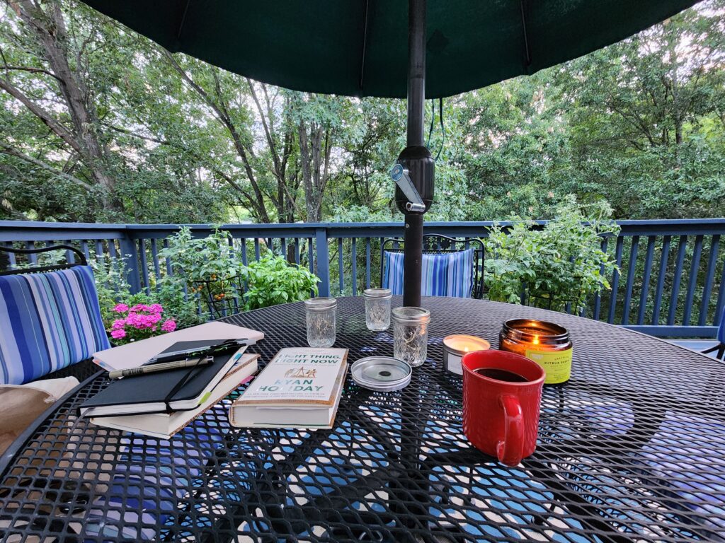 Table on a deck outside with a cup of coffee, a journal, and "Right Thing, Right Now" by Ryan Holiday.