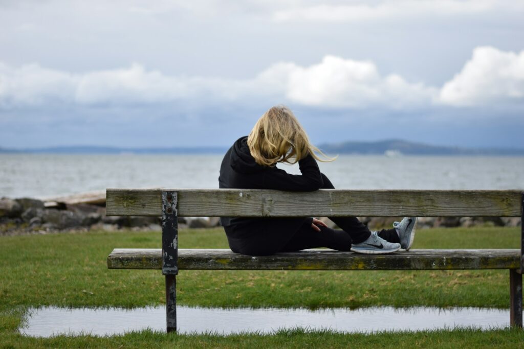 Woman sitting alone on a bench, looking out over calm water, reflecting on life and personal direction