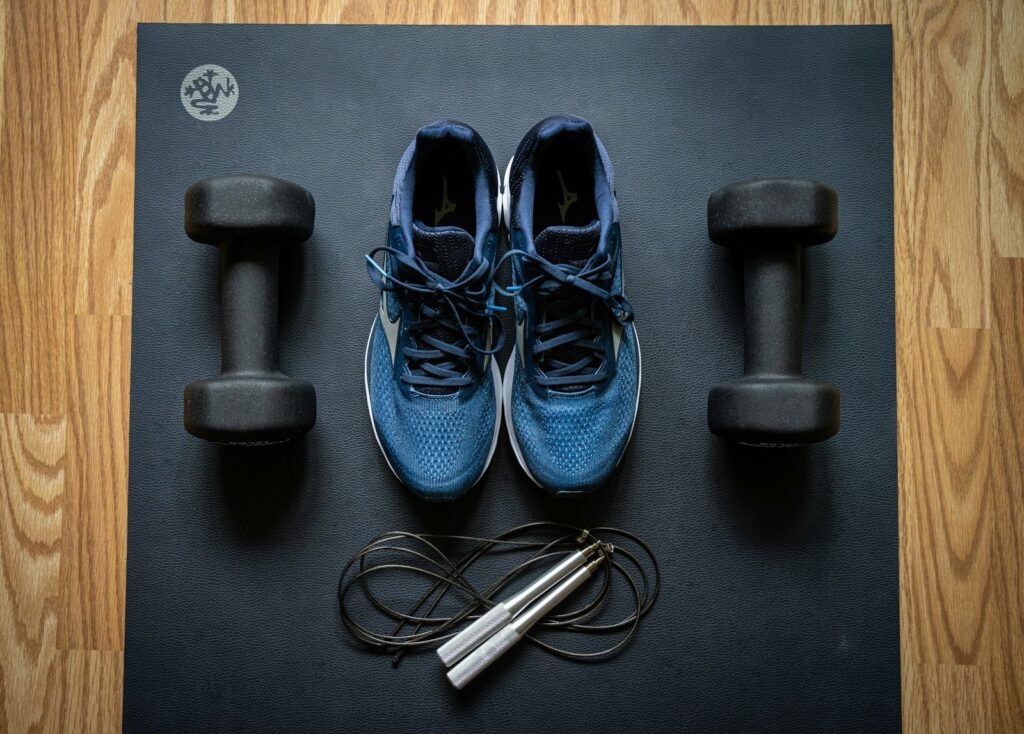 Flat lay of home workout essentials with dumbbells, jump rope, and athletic shoes on yoga mat for strength and cardio training.