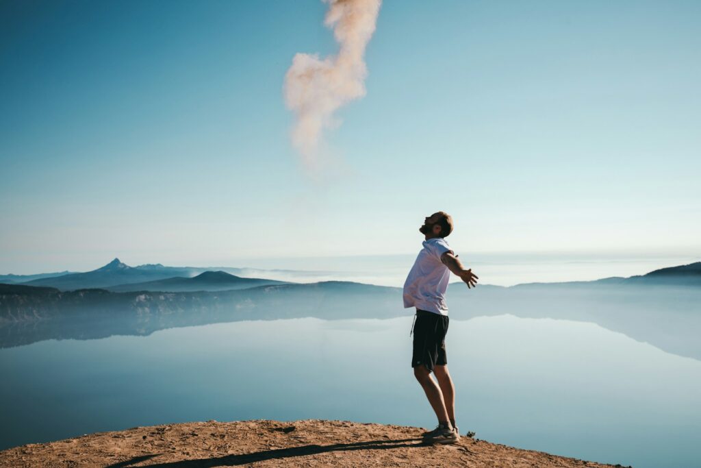 Person standing with arms outstretched on a mountain overlooking a lake, symbolizing freedom, possibility, and financial clarity connected to life goals.