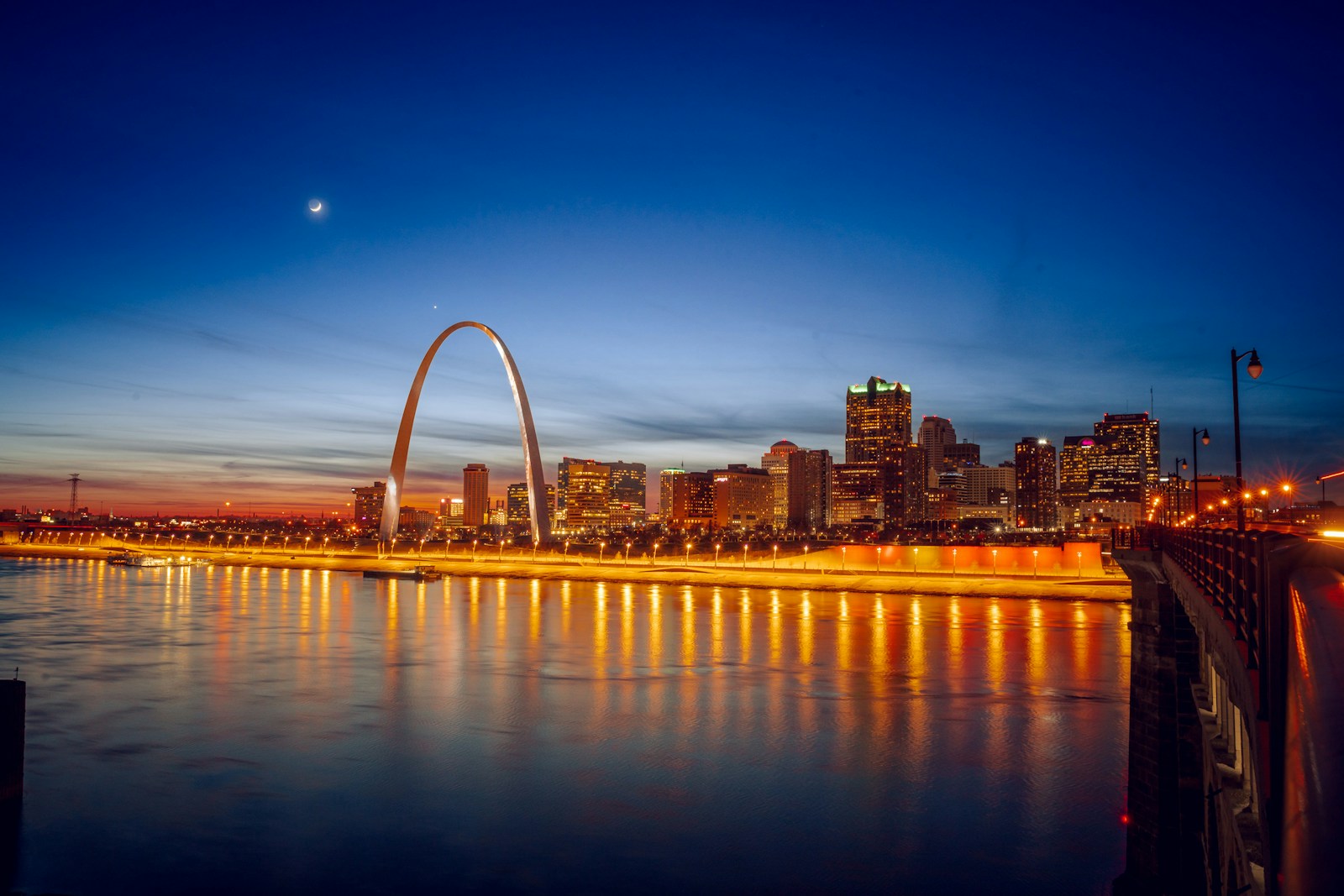 St. Louis Gateway Arch and city skyline illuminated at dusk, reflecting on the Mississippi River.