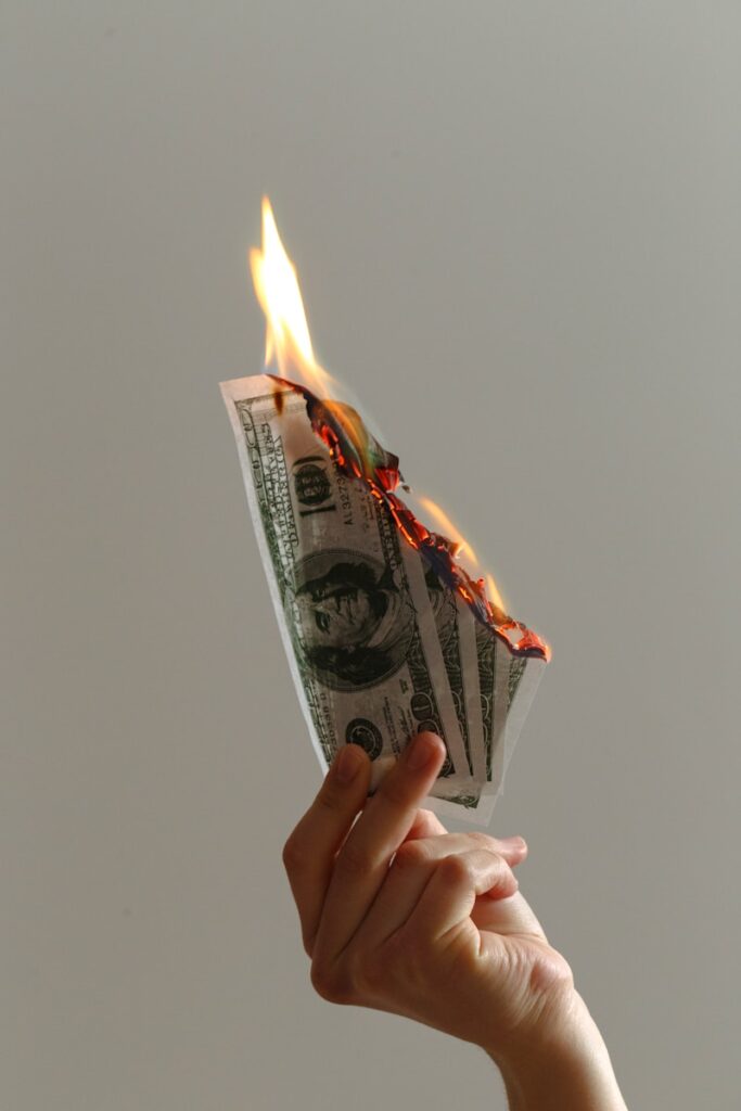 Hand holding burning dollar bills, symbolizing wasted money and the need to identify high-cost financial drains.