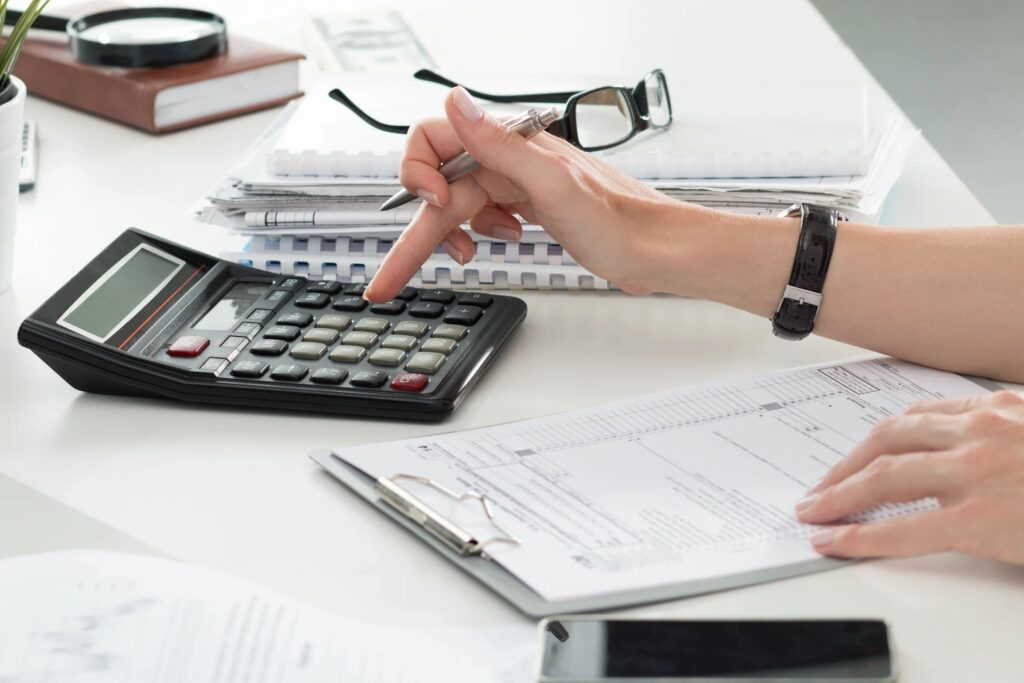 Person using a calculator and writing financial notes on paper, representing tracking assets, liabilities, and net worth.