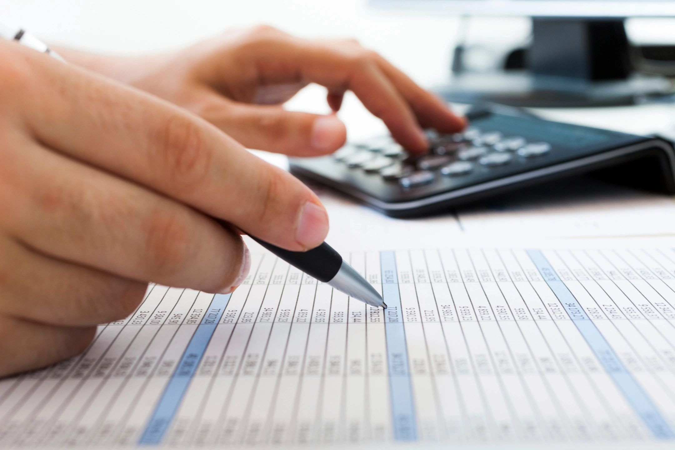 Close-up of a hand holding a pen and reviewing financial numbers with a calculator, symbolizing budgeting and money clarity.