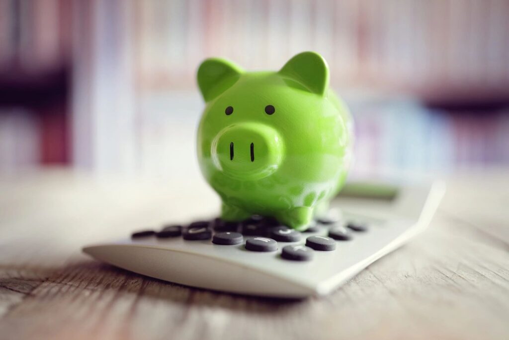 Green piggy bank sitting on a calculator, symbolizing saving money and taking small financial steps toward progress.