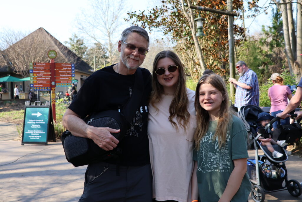 Father, daughter, and granddaughter posing together at the zoo during a family outing