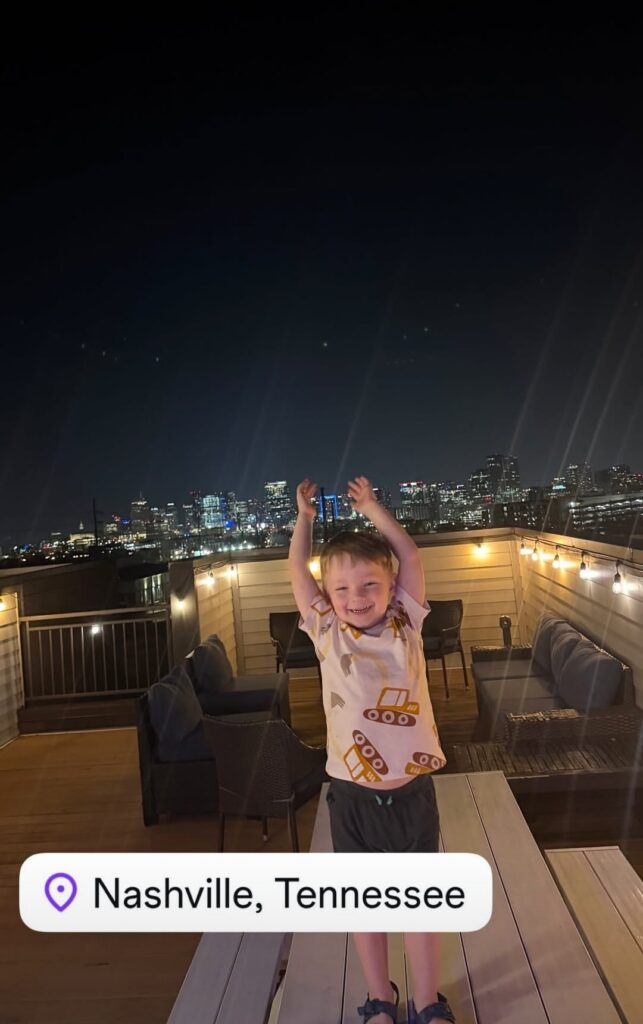 Grandson on rooftop at night with Nashville skyline in the background during a family trip