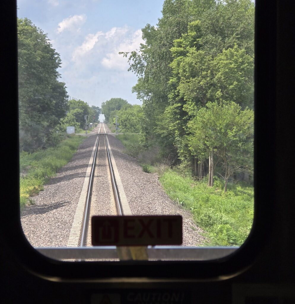 View of the railroad tracks from the back window of the last Amtrak train car traveling to Chicago