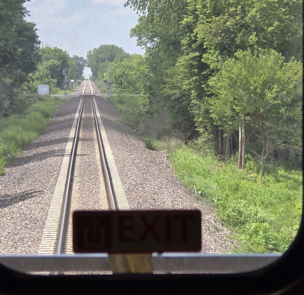 View of the railroad tracks from the back window of the last Amtrak train car traveling to Chicago