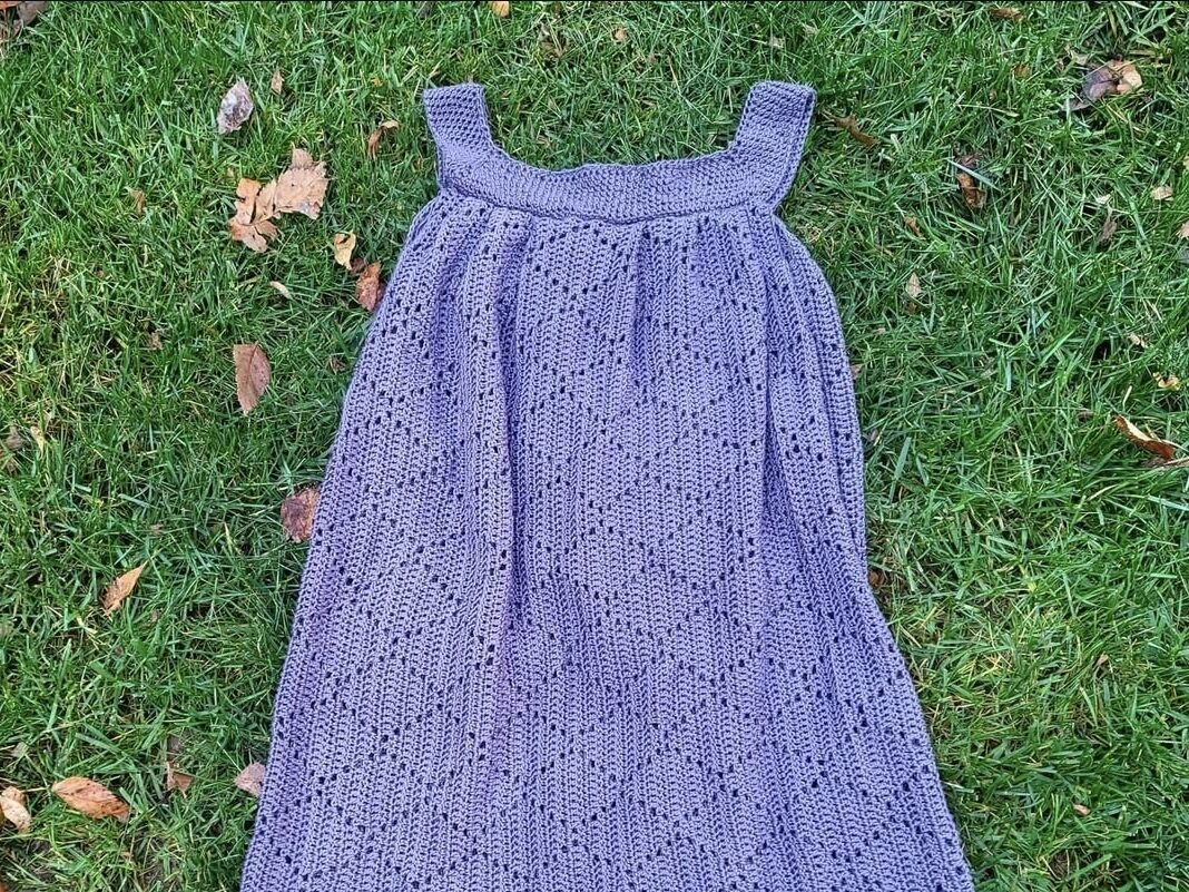 Handmade gray crocheted dress laid on green grass, showcasing creativity and craftsmanship through fiber arts.